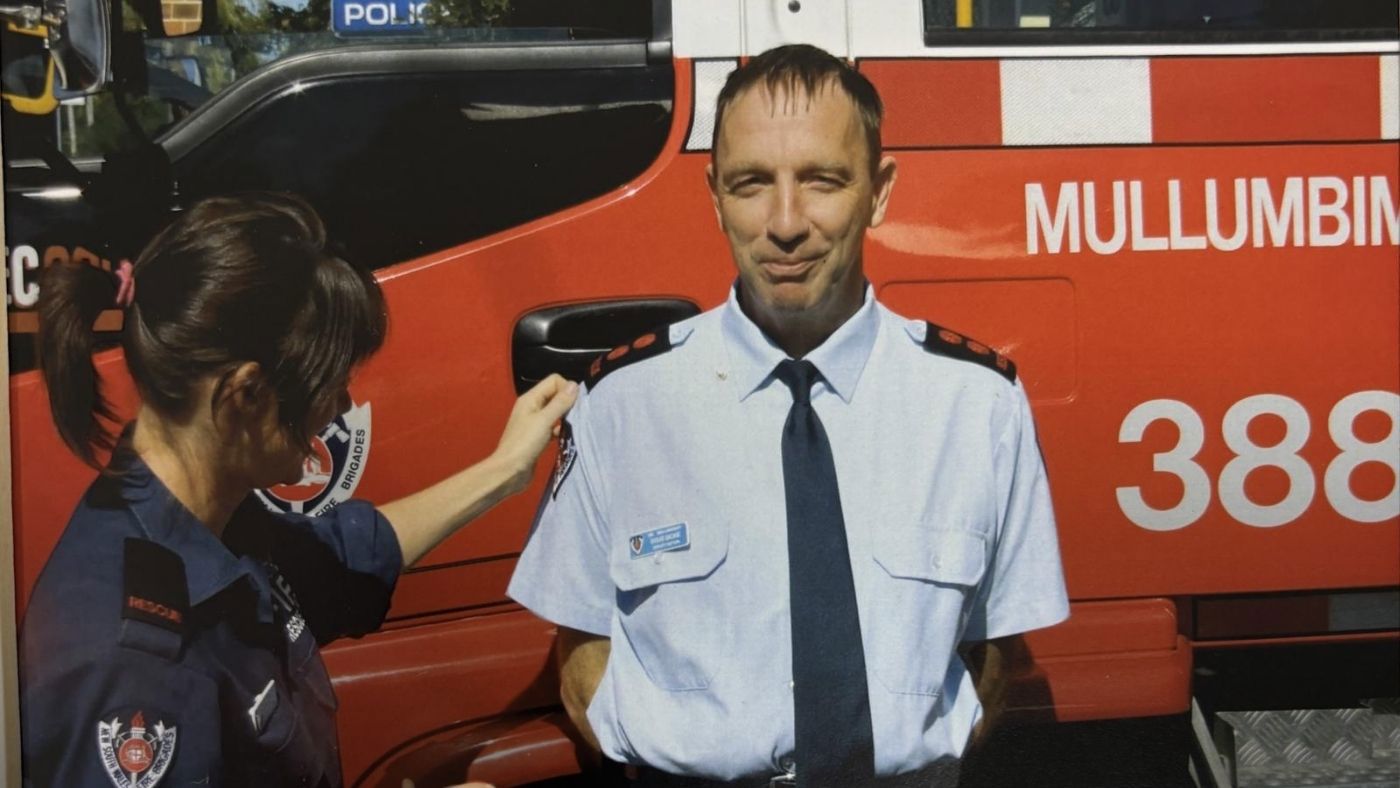 A man standing posing for a photo outside a fire appliance with a woman adjusting his shirt
