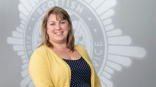 Head and shoulders image of Board member Mhairi Wylie smiling in front of a grey SFRS crest