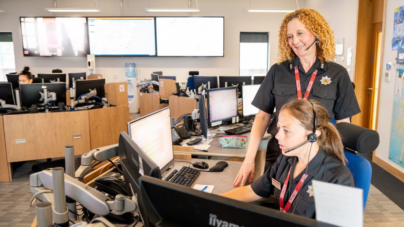 Two firefighters control seated at desks in an emergency control room, actively using computers.