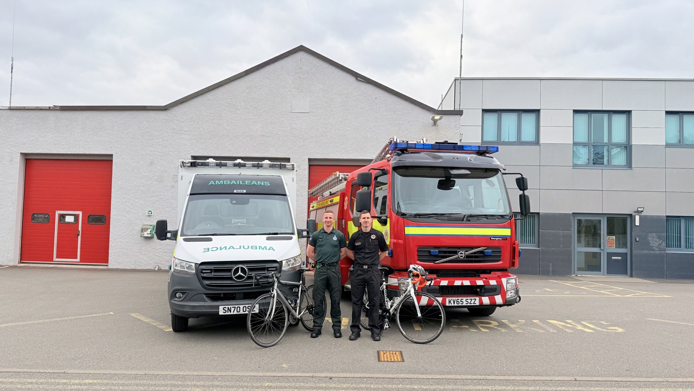 Picture of an ambulance and a fire engine with two men standing in front in emergency service uniform with bikes