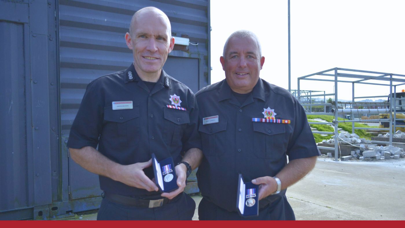Two firefighters in black uniform posing with a medal.