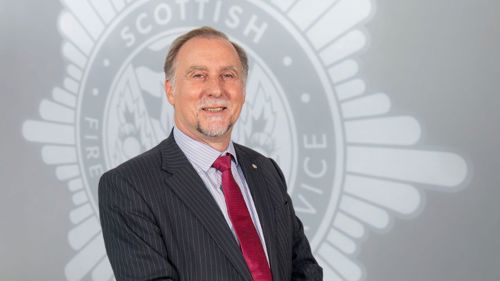 Head and shoulders image of Board member Malcolm Payton smiling in front of a grey SFRS crest