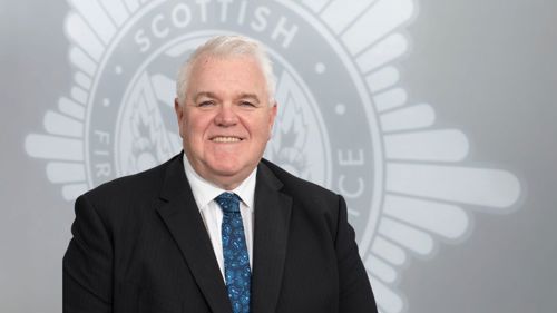 Iain Morris in a suit in front of a grey SFRS crest