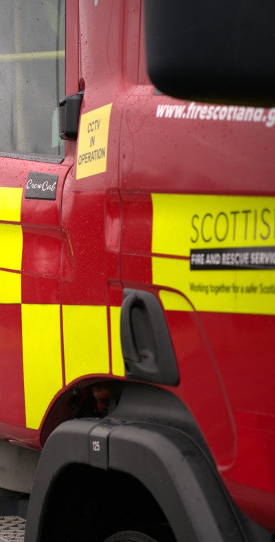 Picture of a fire engine with a firefighter in the background with their hands behind their back.