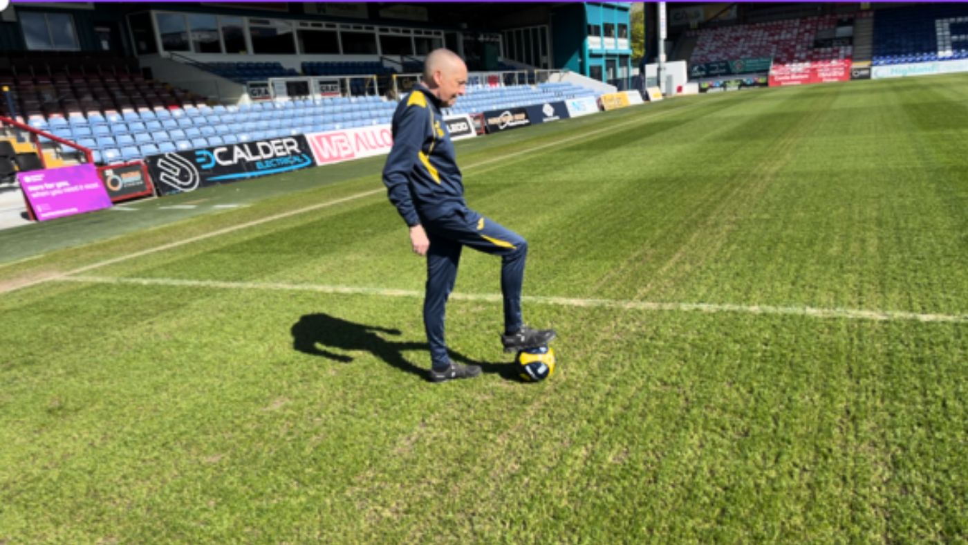 Duncan standing on a football pitch with a football