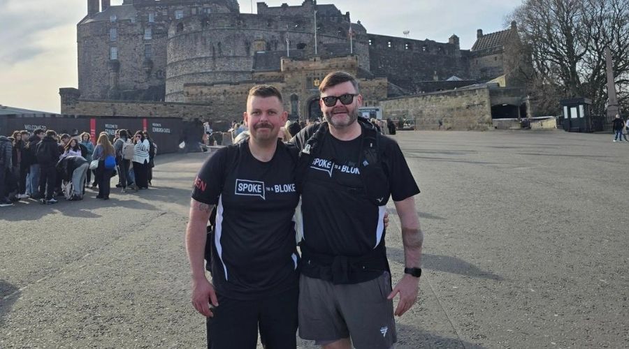 Two men in black shirts stand together in front of Edinburgh Castle
