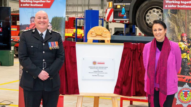  Chief Officer Ross Haggart and Siobhian Brown MSP stand next to a open red curetain exposing a plaque with details of when the building was opened.