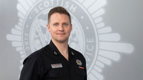 Stuart Stevens in uniform in front of a grey SFRS crest