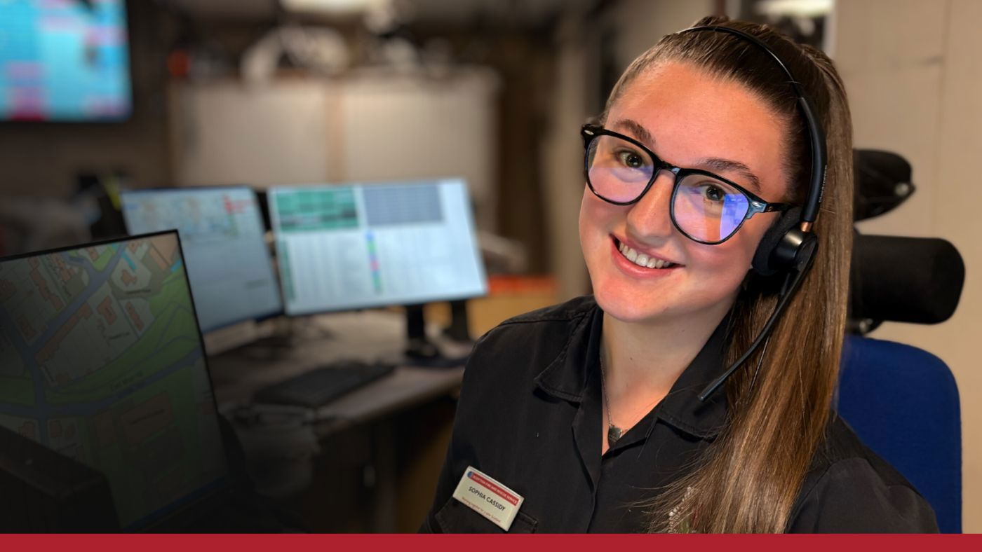 A woman wearing glasses in a black uniform and a headset smiles warmly.