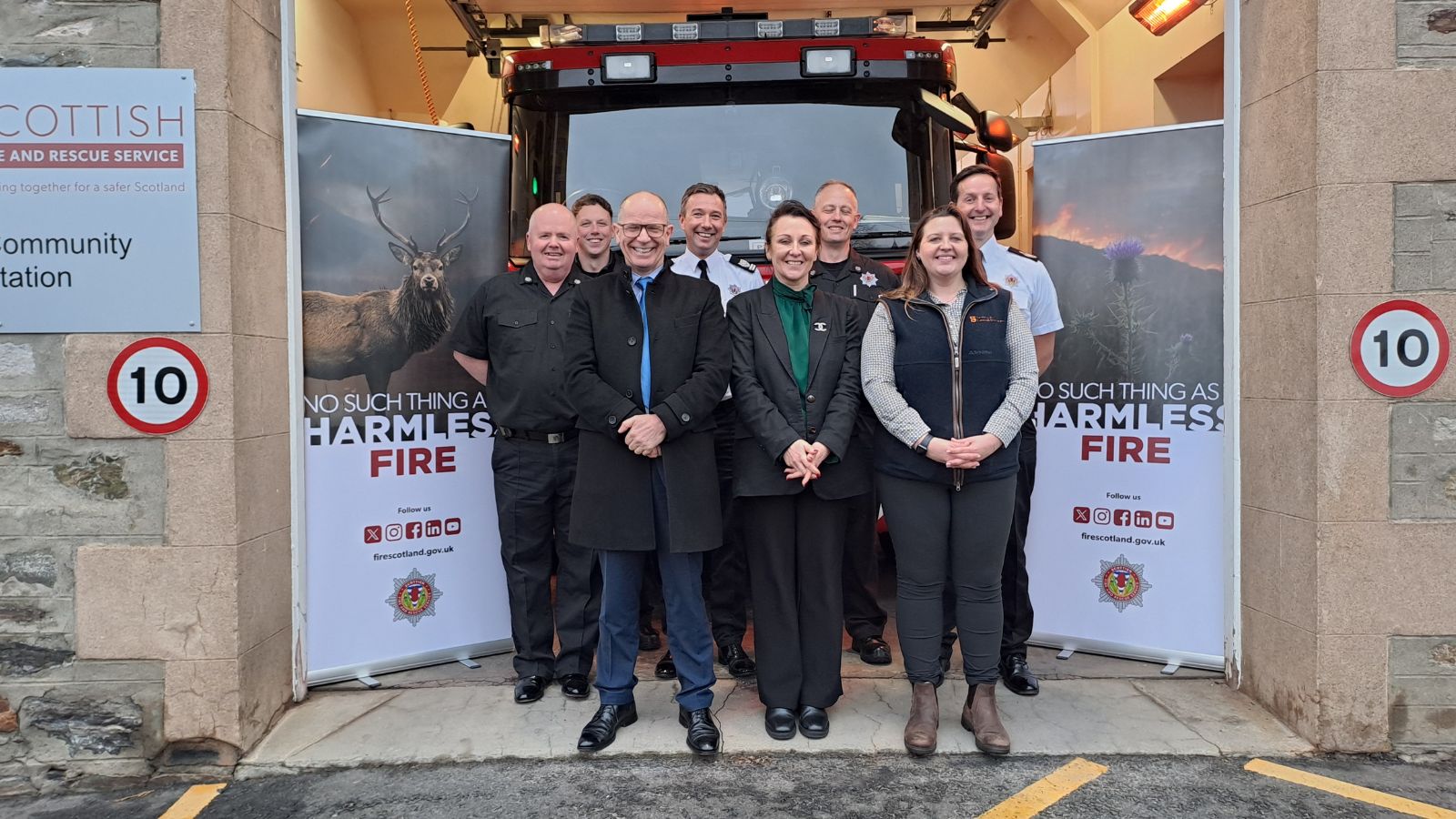 A diverse group of people stands in front of a fire station, smiling and posing for the camera.