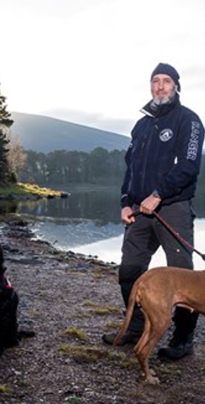 two men and two dogs standing next to a reservoir on a cold day
