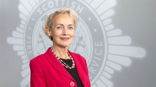 Head and shoulders image of Board member Angiolina Foster smiling in front of a grey SFRS crest