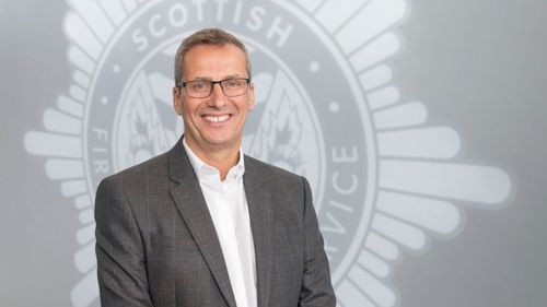 Head and shoulders image of Board member Steve Barron smiling in front of a grey SFRS crest