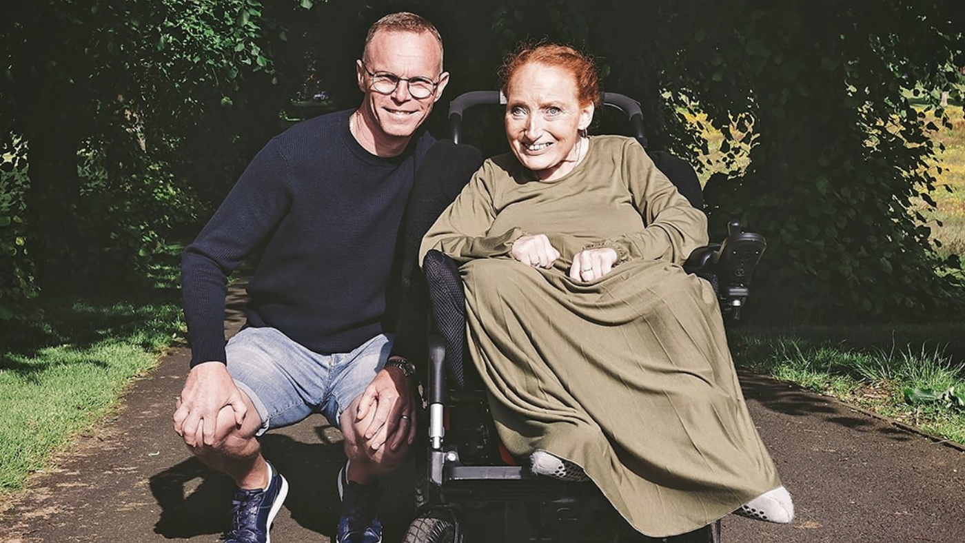 A picture of a man kneeling down next to a woman who is in a wheelchair