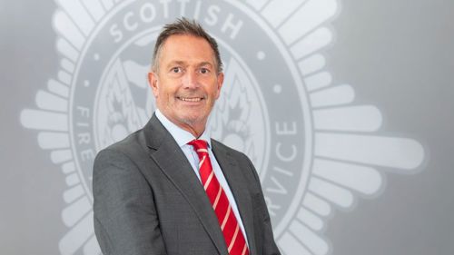 Head and shoulders image of Board member Brian Baverstock smiling in front of a grey SFRS crest