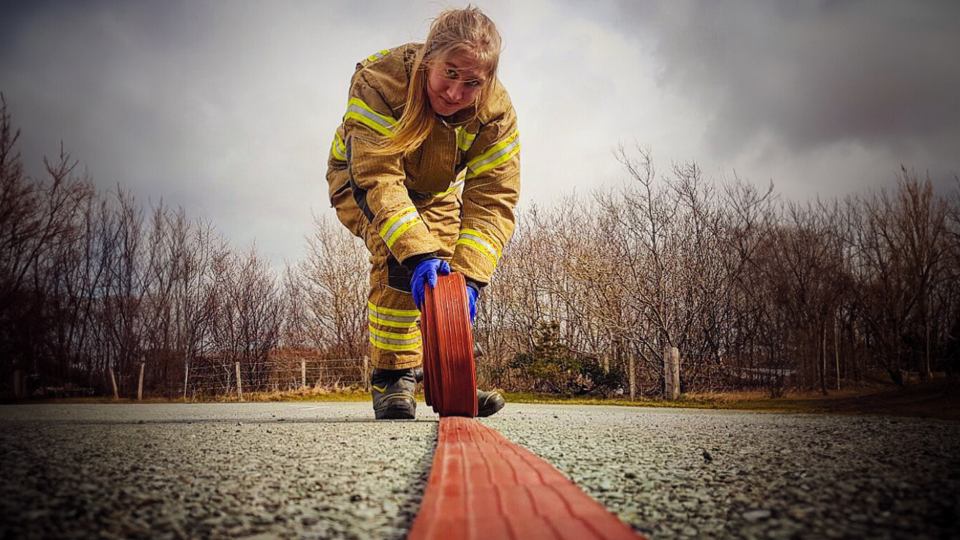 Female firefighter rolling a red hose