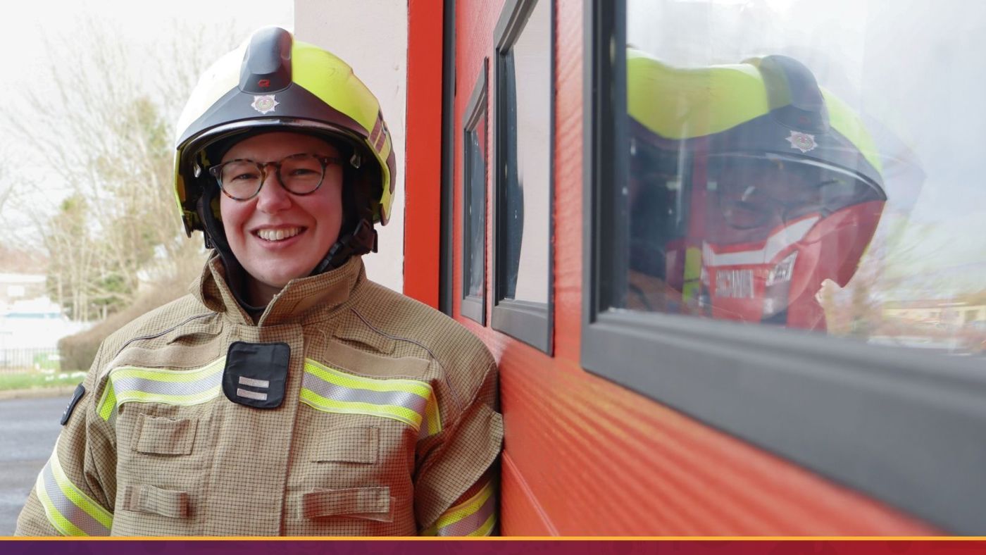 A firefighter with a broad smile peers out of a fire station door, reflecting enthusiasm and commitment to their duty.