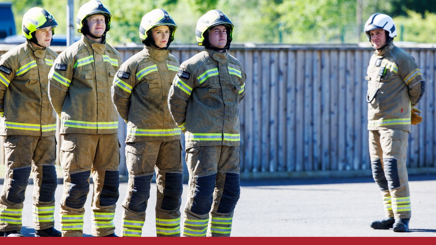 A group of firefighters lined up, wearing helmets and gear.