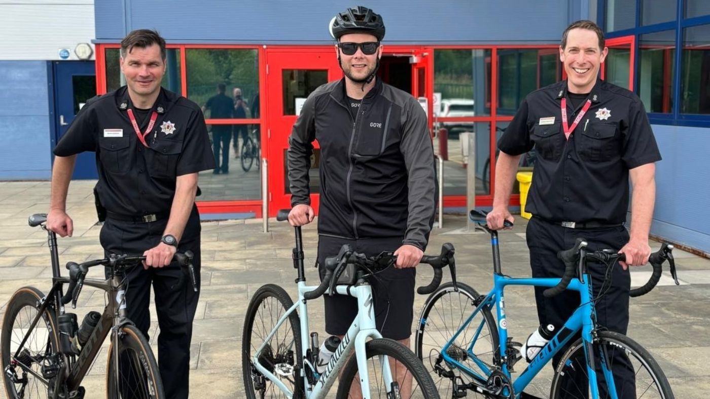 Three men in black shirts uniform standing next to bicycles.