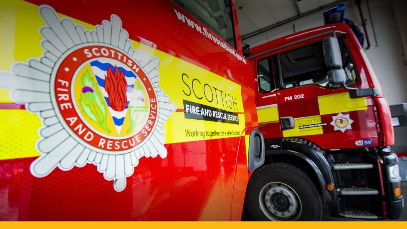 Two fire appliances parked in a garage with a large red and yellow the Scottish Fire and Rescue Service logo.