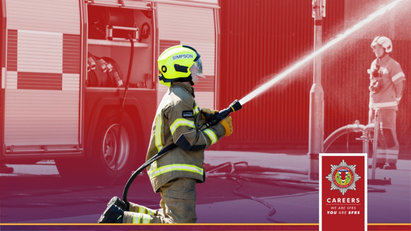 A firefighter uses a hose to spray water, a fire engine is in the background