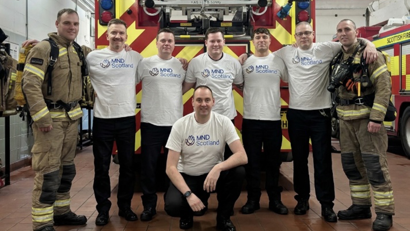 Group of firefighters in fire kit and MND Scotland t-shirts standing in front of fire appliance.