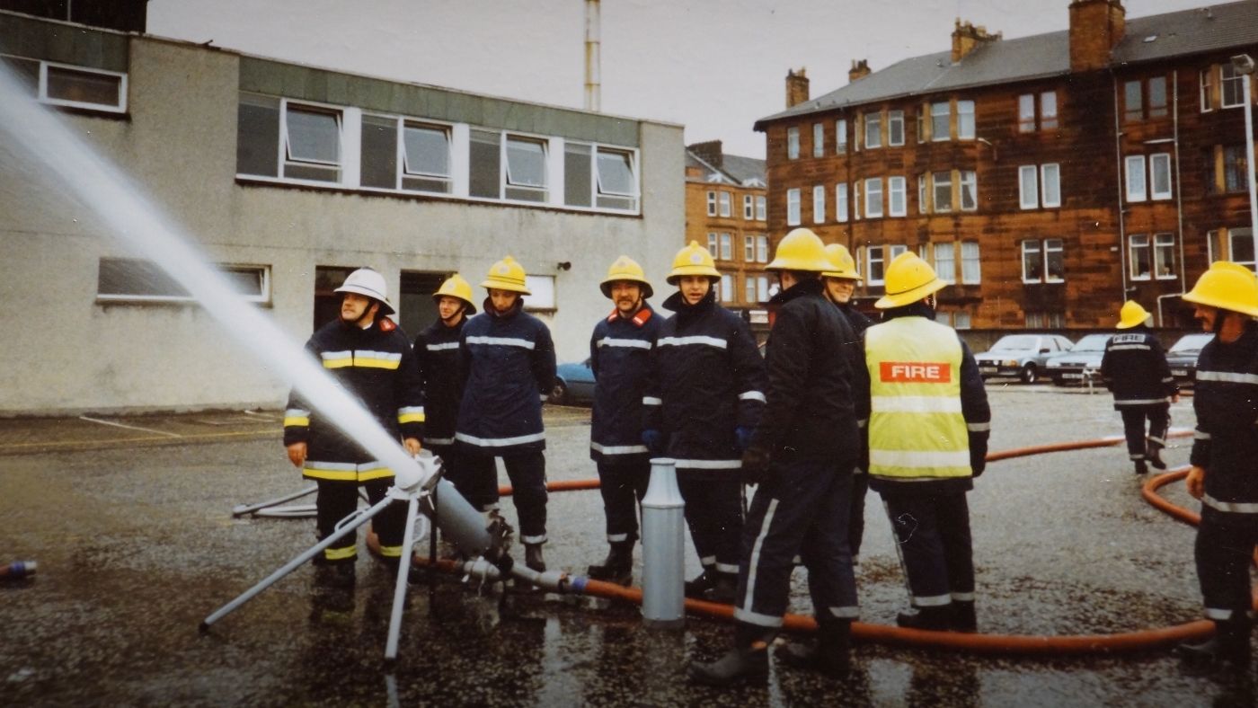 A group of 10 firefighters in Glasgow in full PPE with a hose taking part in a drill