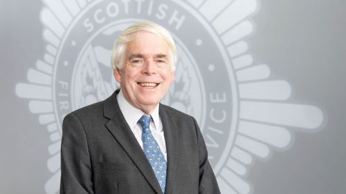 Head and shoulders image of Board member Paul Stollard smiling in front of a grey SFRS crest