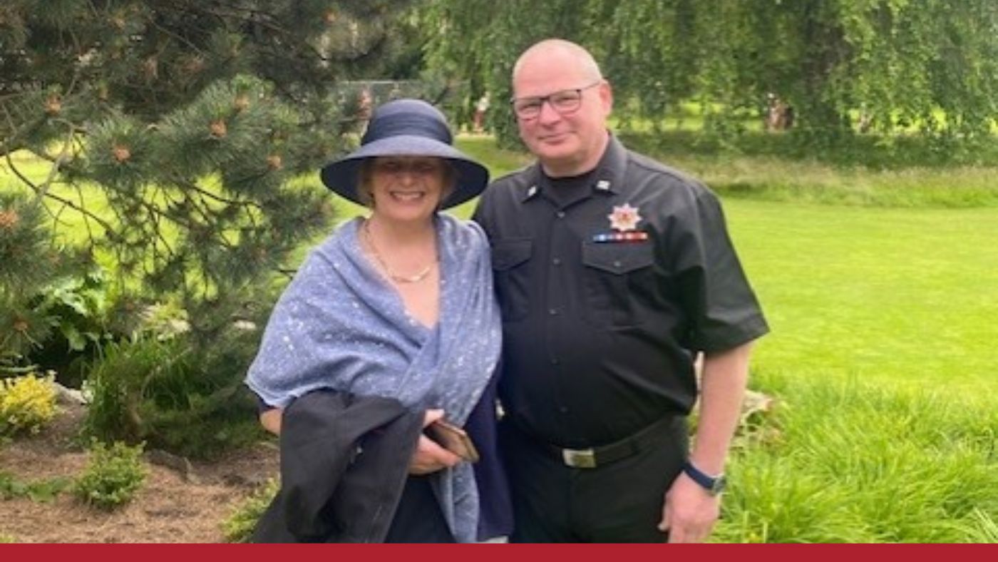 A man and woman pose together in front of a tree, both smiling and dressed casually.