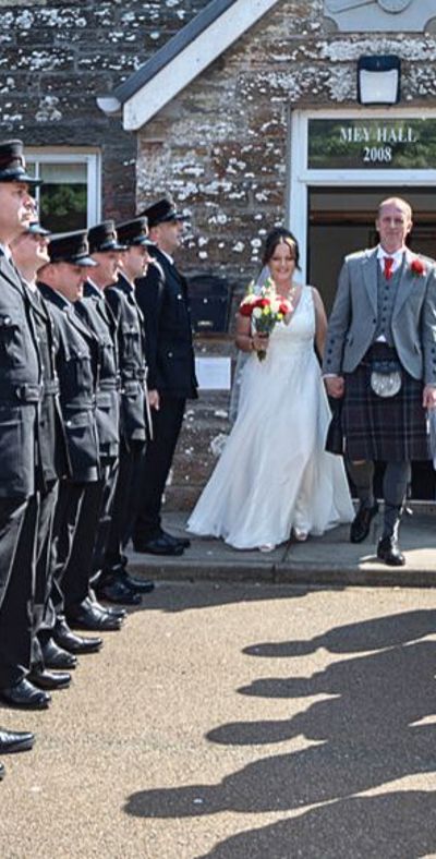 a bride and groom walking out of an old building through a line of firefighteres dressed in black uniforms