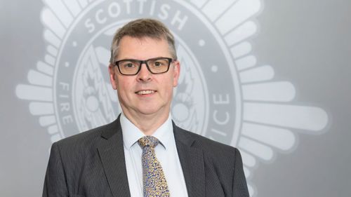 John Thomson in a suit in front of a grey SFRS crest