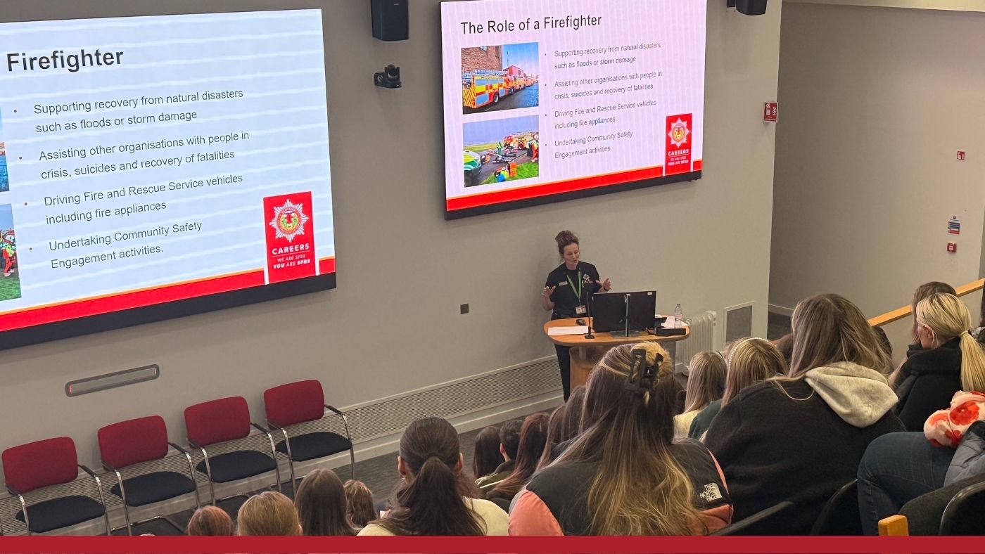 A woman in a black uniform presents on the "Role of a Firefighter" to a classroom.