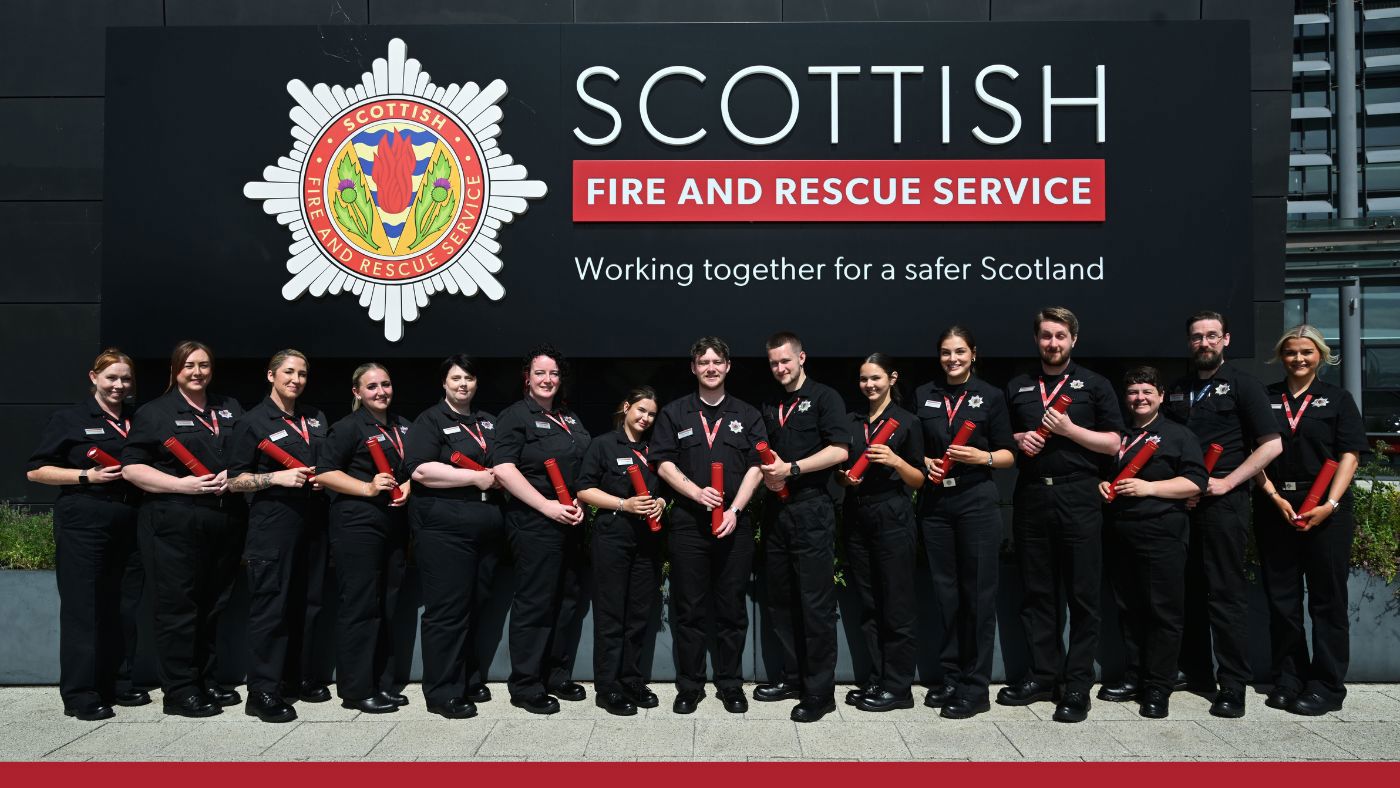 A group of firefighters in black uniform standing in front of a corporate emblem.