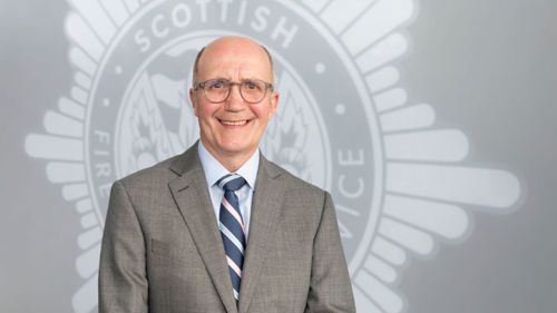 Head and shoulders image of Board member Stuart Ballingall smiling in front of a grey SFRS crest