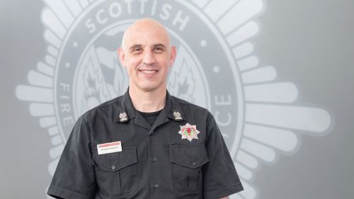 Deputy Assistant Chief Officer Stephen Wright in uniform in front of a grey SFRS crest
